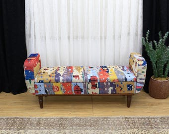 May include: A colorful upholstered bench with a patchwork design. The bench has a wooden frame and legs. The fabric features a variety of colors and patterns, including red, blue, yellow, and orange. The bench is approximately 48 inches long.