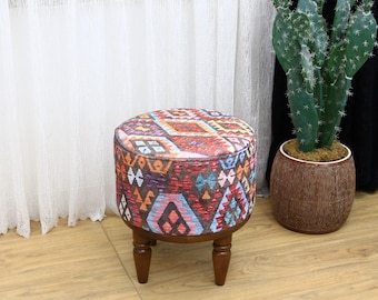 May include: A round, colourful ottoman with a geometric pattern. The ottoman has four wooden legs and is sitting on a wooden floor.