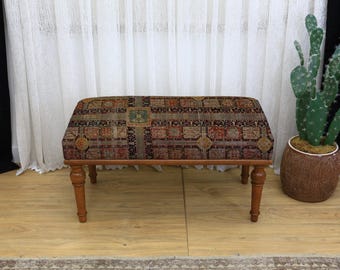 May include: A rectangular upholstered bench with a patterned fabric top in shades of brown, red, and green. The bench has four turned wooden legs and a wooden frame. The bench is approximately 36 inches long, 18 inches wide, and 18 inches high.