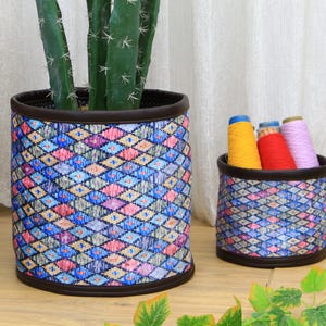 Könnte beinhalten: Zwei bunte Stoffkörbe mit Mustern. Der größere Korb ist mit einer Topfpflanze gefüllt. Der kleinere Korb ist mit bunten Garnen gefüllt.