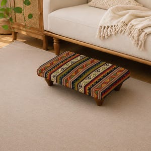 Può includere: Un poggiapiedi rettangolare caratterizzato da un rivestimento in tessuto dai colori vivaci con un motivo geometrico ripetuto nei toni dell'arancione, del verde, del nero e del crema. Il mobile basso poggia su quattro gambe corte in legno scuro.