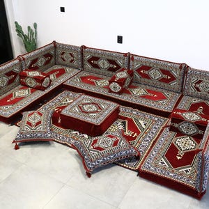 May include: A modular, floor-seating set with a rich red and patterned design. The set includes multiple cushions, backrests, and a central square ottoman. The intricate patterns feature cream, black, and gold accents, creating a luxurious aesthetic.
