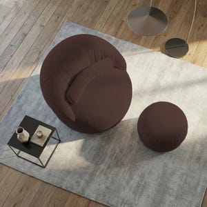 May include: A modern brown armchair with a matching round ottoman, set on a light gray rug. A small black side table with decorative items sits nearby. The chair has a rounded shape and a textured fabric.