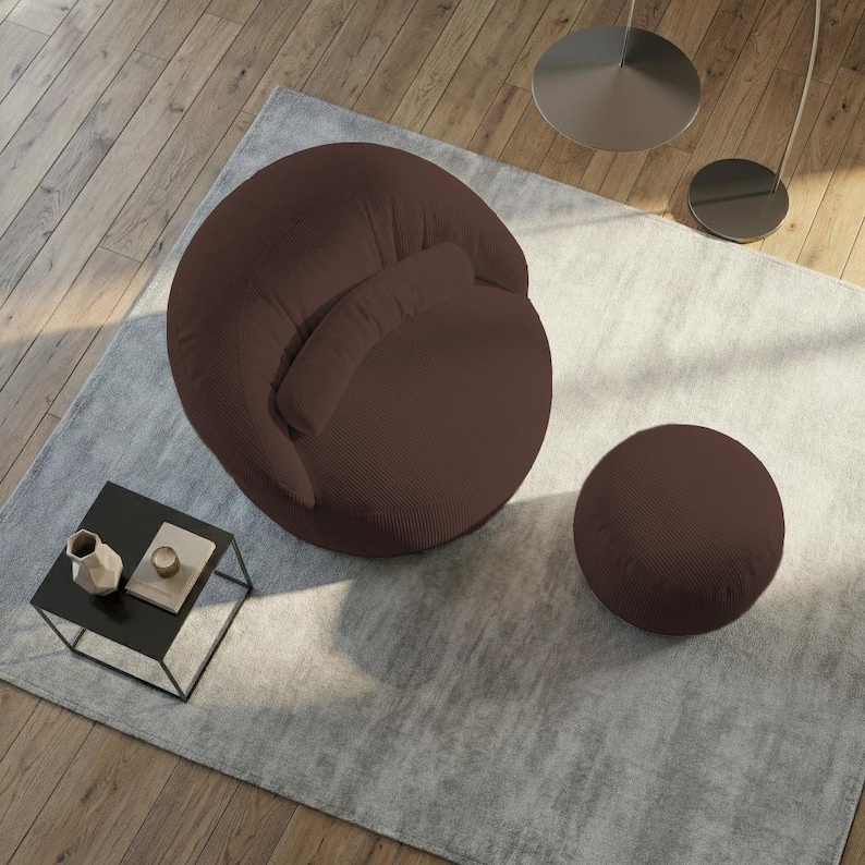 May include: A modern brown armchair with a matching round ottoman, set on a light gray rug. A small black side table with decorative items sits nearby. The chair has a rounded shape and a textured fabric.