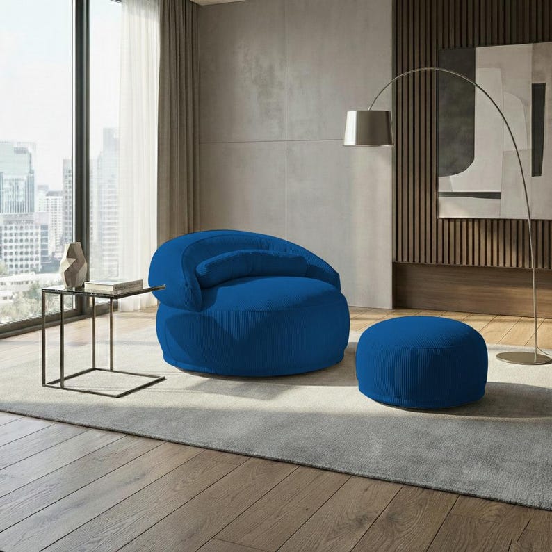 Pu&ograve; includere: Una poltrona blu in velluto a coste con un pouf abbinato. La poltrona ha lo schienale arrotondato e un piccolo cuscino attaccato. Il pouf &egrave; circolare. L'arredamento &egrave; in un salotto moderno.