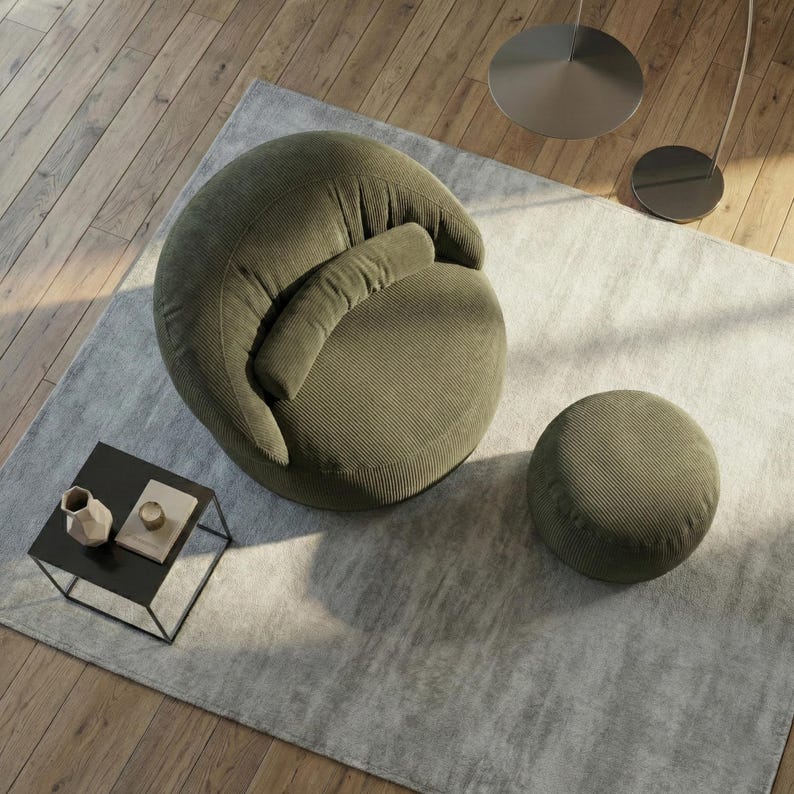 Pode incluir: Uma poltrona de veludo cotel&ecirc; verde-oliva com um pufe a condizer sobre um tapete cinza claro. Uma pequena mesa lateral preta com objetos decorativos est&aacute; em primeiro plano. A cadeira tem uma forma arredondada e um encosto curvo.
