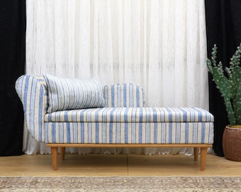 May include: A chaise lounge with a blue and white striped pattern. The wooden frame has four legs. A matching pillow rests on the back. A cactus in a brown pot is to the right.