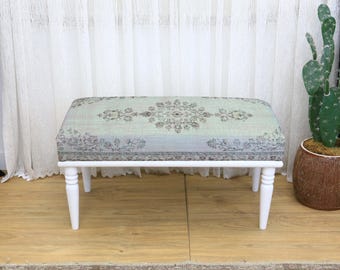 May include: A rectangular bench with a white wooden frame and four legs. The cushioned top features a floral pattern in shades of green, gray, and beige. The bench is approximately 36 inches long.