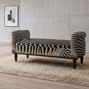 May include: A backless bench featuring a black and white zebra print upholstery. The bench has two rolled arms at each end and is supported by four dark brown wooden legs with a turned design. The seat is rectangular with a continuous striped pattern.