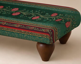 Op de afbeelding: Een rechthoekige gestoffeerde bank met een donkergroene bovenkant en een centraal rankpatroon van roze bloemen. De zijkanten zijn versierd met een veelkleurige rand van rode, paarse en groenblauwe geometrische motieven, rustend op vier donkerbruine houten poten.