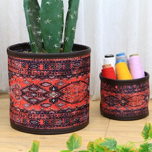 Op de afbeelding: Twee rode en zwarte gepatroneerde opbergmanden van stof. Eén mand is gevuld met kleurrijke garenrollen. De andere mand is leeg en heeft een cactusplant erin.
