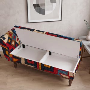May include: A rectangular storage bench featuring a vibrant, multi-colored geometric pattern in red, blue, yellow, and cream. The bench has a hinged lid that opens to reveal two white interior storage compartments and stands on four dark wooden legs.