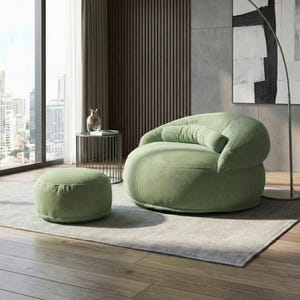 Pode incluir: Uma cena de sala de estar moderna com uma poltrona de veludo cotel&ecirc; verde claro e um pufe a condizer. A cadeira arredondada tem encosto e apoio de bra&ccedil;os curvos. O pufe &eacute; circular. A sala tem uma janela grande, uma mesa lateral e um tapete neutro.