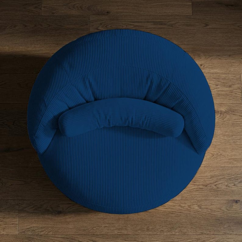 Pu&ograve; includere: Vista dall'alto di una poltrona in velluto a coste blu navy. La sedia ha una forma arrotondata con schienale curvo e un piccolo bracciolo imbottito. Il tessuto di velluto a coste presenta delle scanalature verticali e la sedia &egrave; su un pavimento in legno.