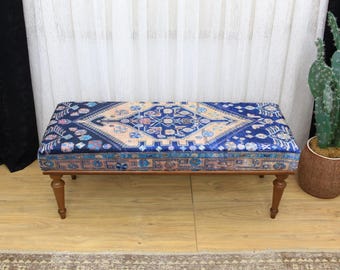 May include: A wooden bench with a blue and beige patterned cushion. The bench has four legs and is sitting on a wooden floor.