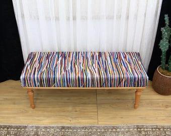 May include: A wooden bench with a colorful striped fabric seat. The bench has a simple design with four legs and a rectangular seat.