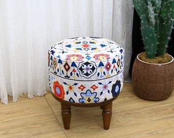 Könnte beinhalten: Ein runder, weißer Hocker mit einem bunten, geometrischen Muster. Der Hocker hat vier Holzbeine und steht auf einem Holzboden.