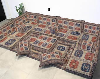 Può includere: Set di sedute modulari da pavimento con un motivo geometrico beige, rosso e blu. Il set comprende più cuscini ed elementi da pavimento, creando una disposizione di sedute a basso profilo. Il design presenta un'estetica tradizionale simile a un tappeto.