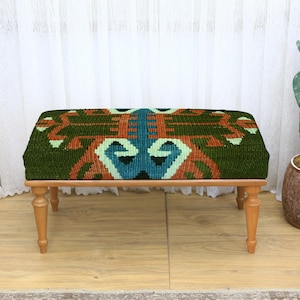 May include: A rectangular ottoman with a patterned top in shades of green, orange, and teal. The wooden legs are light brown. The ottoman is a decorative piece of furniture.
