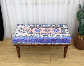 May include: A blue and pink patterned ottoman with wooden legs. The ottoman is sitting on a wooden floor.