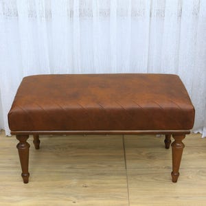 May include: A brown leather bench with a diamond-stitched pattern on the top and wooden legs.
