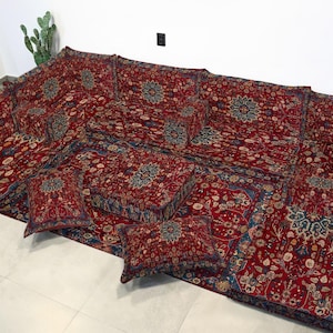 May include: A large, modular seating set with a rich red and blue floral pattern. The set includes a large base, backrests, and several matching throw pillows. The design is reminiscent of traditional oriental rugs, creating a cozy and inviting space.