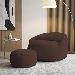 Pu&ograve; includere: Una poltrona a sacco in velluto a coste marrone con un pouf abbinato. La sedia ha lo schienale arrotondato e un cuscino rettangolare. Il pouf &egrave; circolare. I mobili sono su un tappeto grigio.