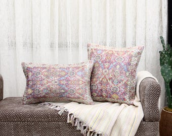 May include: Two decorative throw pillows with a colorful floral pattern on a brown couch with a white throw blanket.