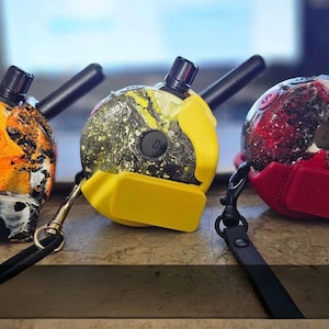 May include: Three colorful, patterned electronic devices with antennas and attached lanyards. The devices have a round shape with a black top and a small screen. One is orange and black, another yellow and black, and the third red and black.