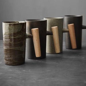 Puede incluir: Cuatro tazas de cerámica con asas de madera. Las tazas son de diferentes tonos de marrón y verde. Las asas son todas del mismo color y están hechas de madera.