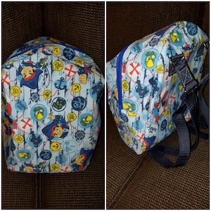 Puede incluir: Mochila azul claro con un estampado de temática pirata. El diseño incluye piratas de dibujos animados, mapas del tesoro, anclas y monedas de oro. La mochila tiene una cremallera azul y correas ajustables.