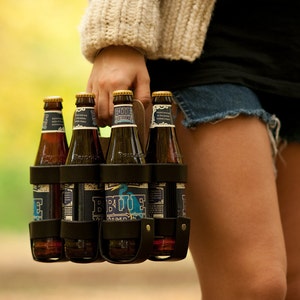 A woman holding a 6-pack of beer in a handsome leather and wood reusable 6-pack carrier