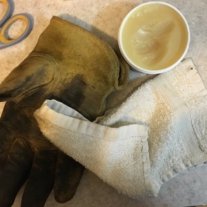 May include: A close-up of a brown leather work glove, a white towel, and a container of leather conditioner.