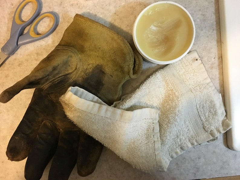 May include: A close-up of a brown leather work glove, a white towel, and a container of leather conditioner.