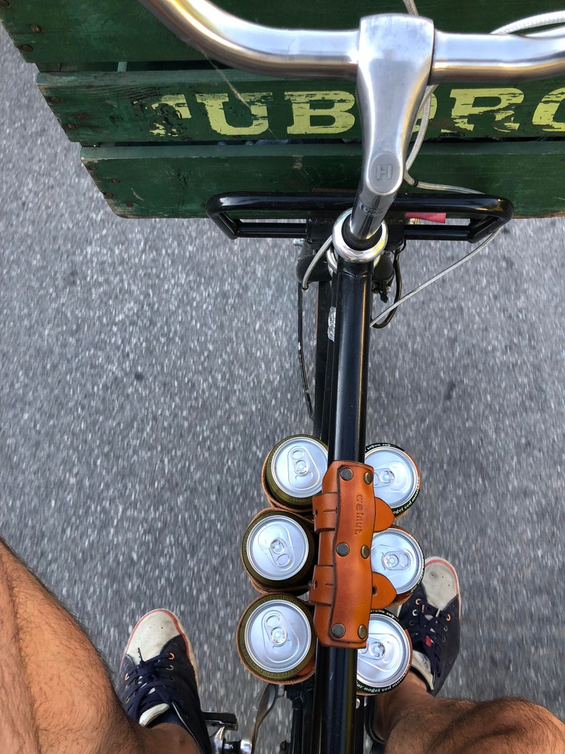 Customer photo looking down on the top tube of a bicycle from the saddle with their feet on the pedals. The street below is in motion and the top tube is holding a 6-pack of beer with a leather carrying strap