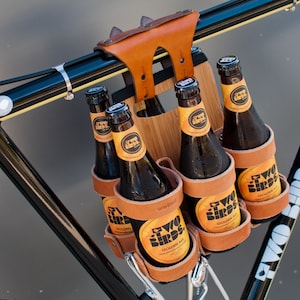 Honey leather and bamboo six-pack held on the top tube of a black bicycle with a 6-pack beer carrier, the 6-pack frame cinch on a custom branded bike for an Australian brewery