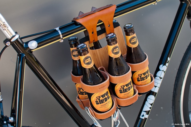 Honey leather and bamboo six-pack held on the top tube of a black bicycle with a 6-pack beer carrier, the 6-pack frame cinch on a custom branded bike for an Australian brewery