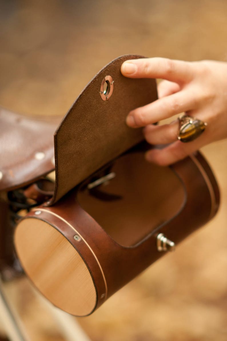 Hand opening dark brown leather barrel bag attached to saddle to demonstrate hole opening size