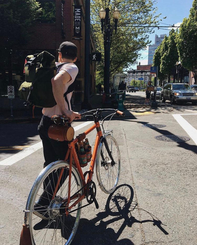 Customer photo of a bicycle being walked across a street intersection with a 6-Pack strapped to the top tube of the bicycle with a bicycle beer carrier combo in Portland Oregon