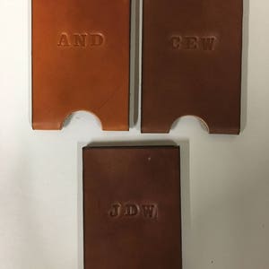 Three examples of monogramming shown clockwise: "AND" on honey leather and "CEW" and "JDW" on dark brown leather wallets