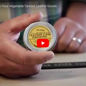 May include: A small tin container of walnut leather care dressing. The tin is yellow with black text that reads "Walnut All Natural Leather Care Dressing".