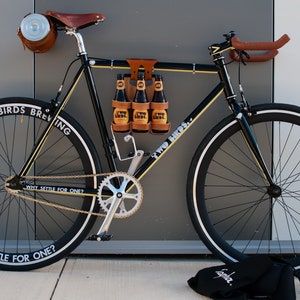 Honey leather and bamboo six-pack held on the top tube of a black bicycle with a 6-pack beer carrier, the 6-pack frame cinch on a custom branded bike for an Australian brewery