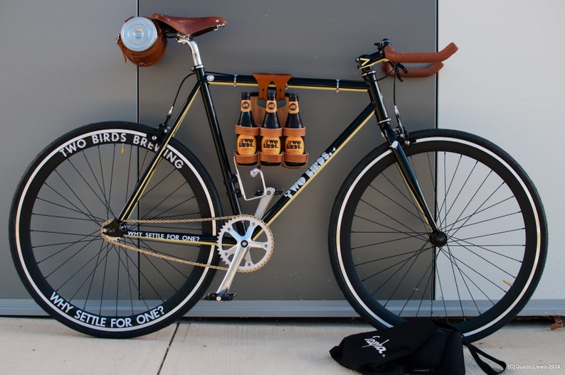 Honey leather and bamboo six-pack held on the top tube of a black bicycle with a 6-pack beer carrier, the 6-pack frame cinch on a custom branded bike for an Australian brewery