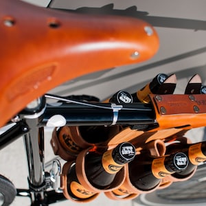 Honey leather and bamboo six-pack held on the top tube of a black bicycle with a 6-pack beer carrier, the 6-pack frame cinch on a custom branded bike for an Australian brewery