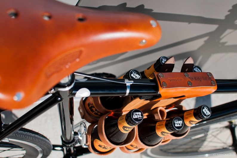 Honey leather and bamboo six-pack held on the top tube of a black bicycle with a 6-pack beer carrier, the 6-pack frame cinch on a custom branded bike for an Australian brewery