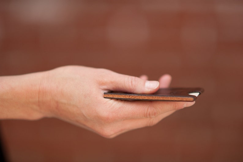 Hand holding minimalist leather card wallet to showcase walnut wood center