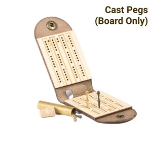 Folding leather travel cribbage board, open and unhinged, showing cast metal pegs in brass and black finishes in peg holes, and an uncorked brass tube that stores the pegs inside the hinge.