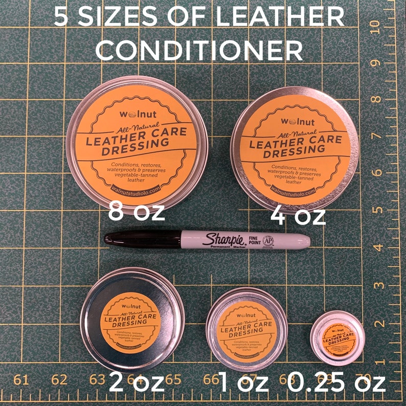 May include: Five different sizes of leather care dressing in metal tins. The tins are labeled "Walnut All-Natural Leather Care Dressing". The tins are arranged from largest to smallest, with the largest tin being 8 ounces and the smallest tin being 0.25 ounces.