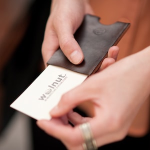 Person pulling "walnut studiolo" business card out of leather business card case