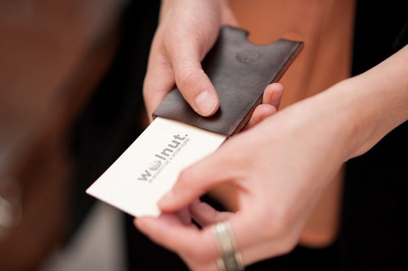 Person pulling "walnut studiolo" business card out of leather business card case